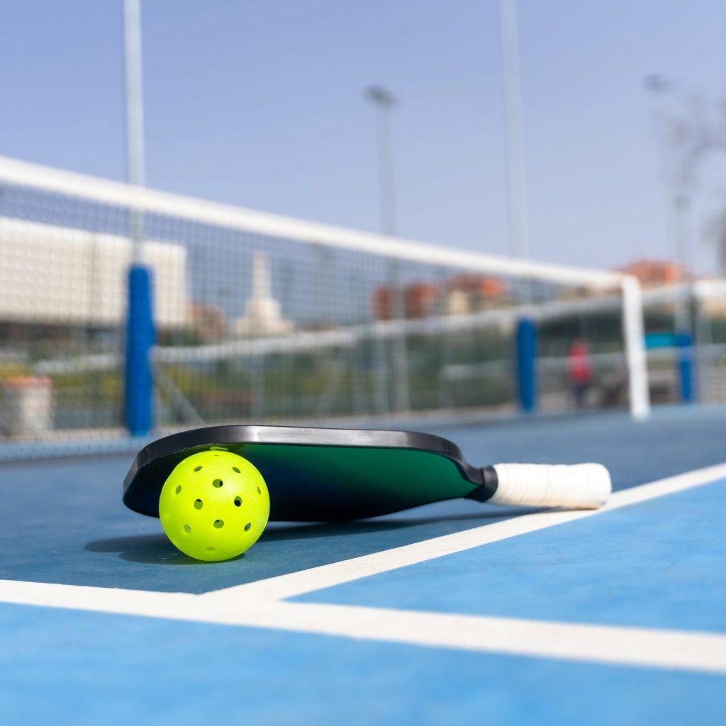 Horizontal photo of a pickleball ball and racket on the ground of a court with no people